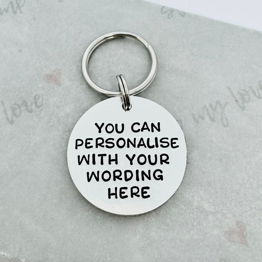 Round personalised hand stamped aluminium keyring with custom wording example on a white background with silver keyring attachment.